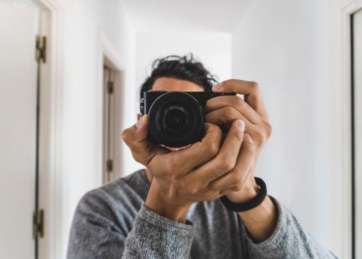 Young man photographer making a selfie at mirror in a white background