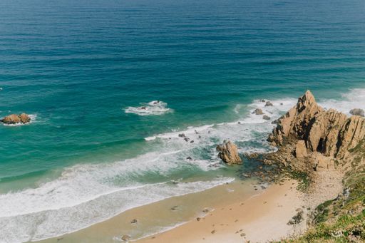A picturesque landscape of a sandy beach situated at the edge of a rocky cliff overlooking the sea