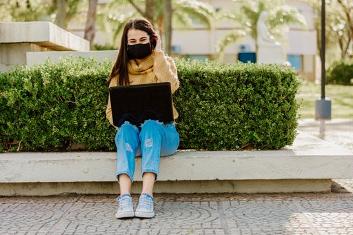 A young Argentinian female student wearing a yellow sweater sitting on a bench with laptop on her legs