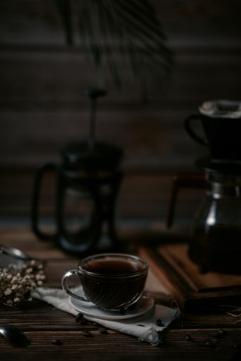 A vertical shot of a cup of coffee with pots on a wooden table with a dark blurry backgroun