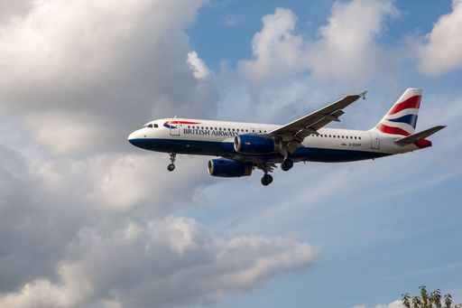 A British Airways airliner soaring through a blue sky with fluffy white clouds in London, UK.