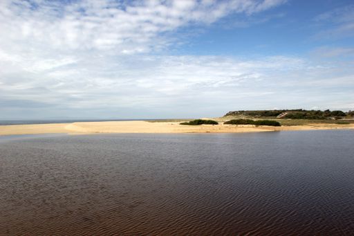 A landscape of the sea surrounded by a beach under the sunlight and a blue cloudy sky