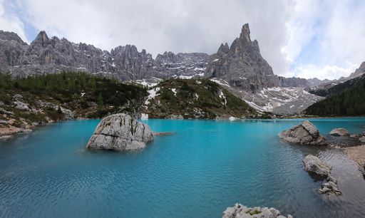 A scenic view of Lake Carezza in the Dolomites, Italy on a cloudy day with the sun peeking through the clouds