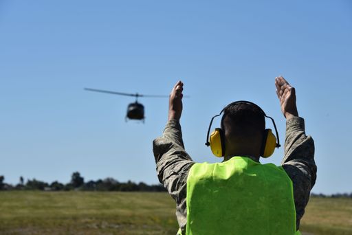 A person standing in an open field with a view of a helicopter flying in the sky above.