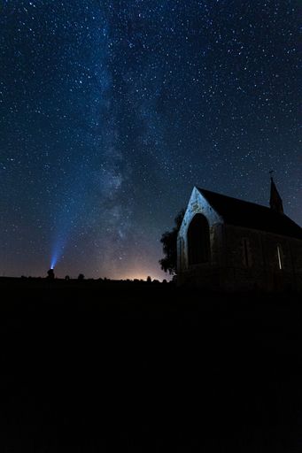 A beautiful silhouette of a church against a night sky illuminated by a bright beam of light.
