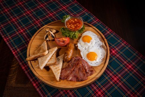 A top-view o delicious full Irish breakfast with sausages, bacon, fried eggs, toasts, and beans