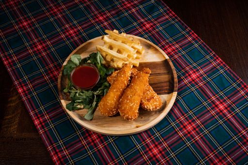 A top-view of crispy chicken nuggets with chips and ketchup on a wooden board on a checkered tablecloth