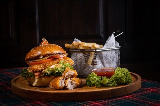 A juicy chicken burger with fresh lettuce and crispy french fries on a wooden board