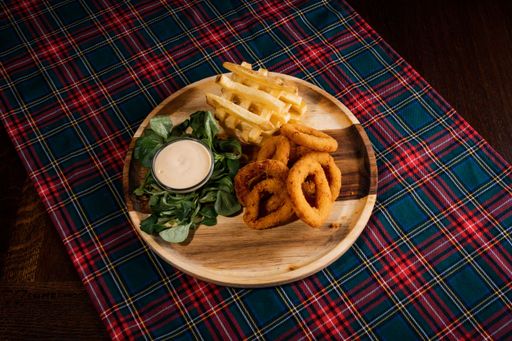 A top-view of delicious crispy onion rings and chips with sauce on a rustic wooden board on a checkered tablecloth