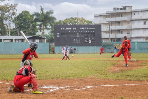 A group of people playing baseball on a green field with a scoreboard visible in the background