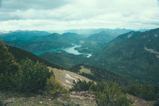 A high angle shot of a beautiful mountainous landscape with green trees and a lake under a cloudy sky