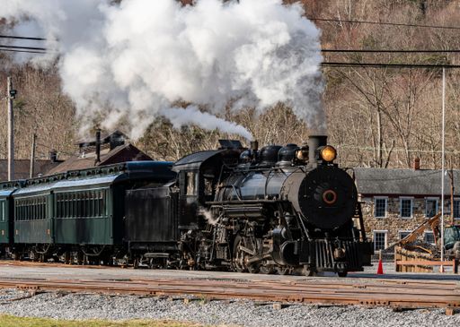 A Front to the Side View of a Restored Narrow Gauge Passenger Train Moving Slowly Thru the Train Yard on a Sunny Morning