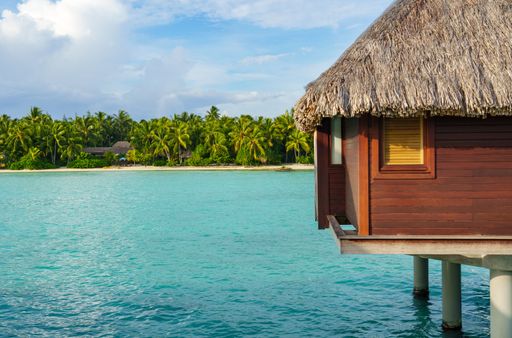 An idyllic tropical paradise featuring crystal-clear blue waters and traditional thatched huts on the shoreline of Bora Bora