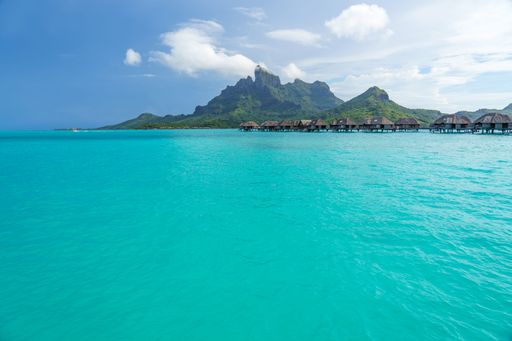 An idyllic tropical paradise featuring crystal-clear blue waters and traditional thatched huts on the shoreline of Bora Bora