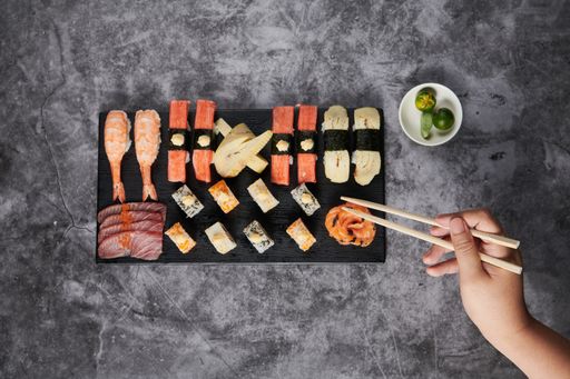 A top view of delicious sushi served on a black wooden plate with chopsticks