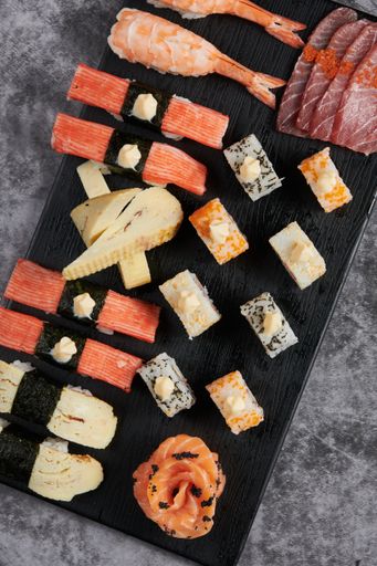 A vertical top view of delicious sushi served on a black wooden plate