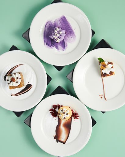 A vertical top view of small cakes served on decorated plates on a minty background