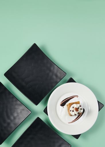 A vertical top view of a small cake served on a decorated plate on a minty background