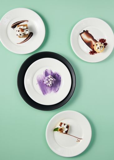 A vertical top view of small cakes served on decorated plates on a minty background
