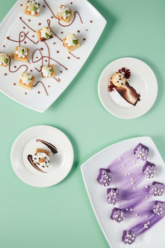 A vertical top view of small cakes served on decorated plates on a minty background
