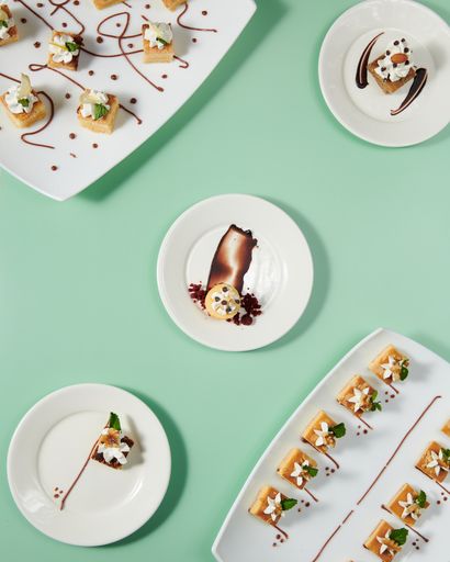 A vertical top view of small cakes served on decorated plates on a minty background