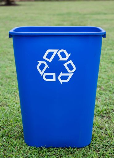 A blue trash can placed on a grassy outdoor