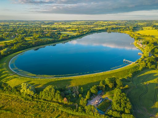 A scenic landscape featuring a tranquil lake surrounded by rolling green hills and lush foliage in Shustoke Reservoir, Birmingham
