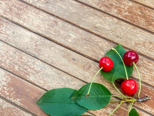 The three cherries lie next to green leaves on a wooden table
