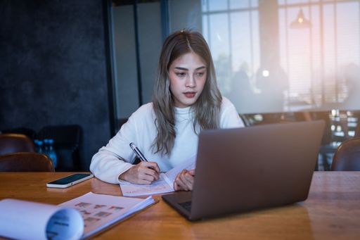 A young woman taking notes while looking at her laptop