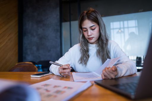 A female working at a desk, using her laptop and notebook