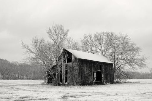 A grayscale shot of an abandoned wooden barn with a surface covered with snow during winter