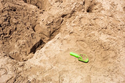 A green plastic toy shovel in the sand on the beach.