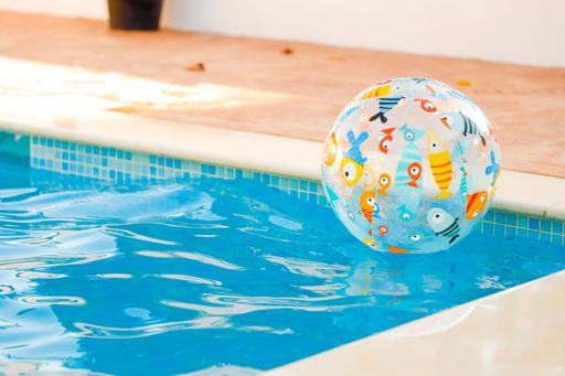 A clear pool ball with cartoon fishes on it in a swimming pool