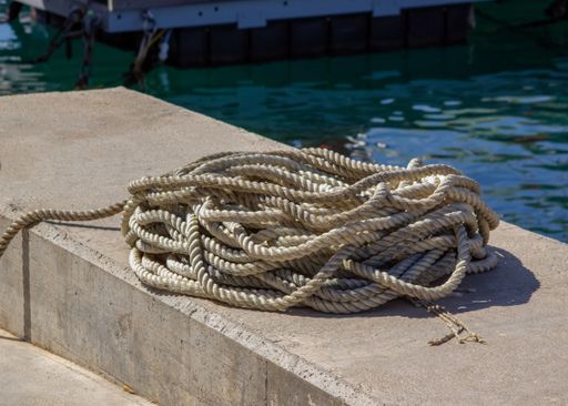 A coiled rope lies on a block near a tranquil lake under the sun
