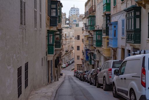 A deserted alleyway featuring an array of parked vehicles, including cars and vans, aligned in a row along both sides of the street