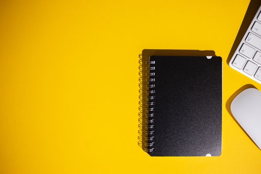 A top view of a notepad, keyboard and a mouse on a yellow work table