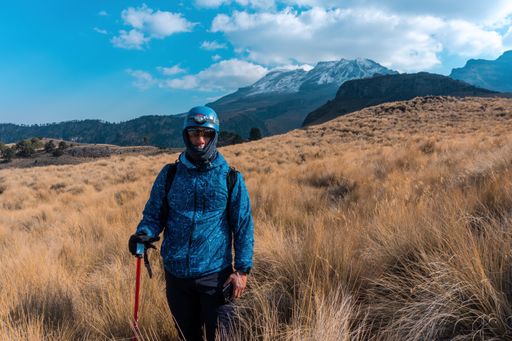 A man standing in a dry grassy field with the Iztaccihuatl volcanic mountain in the background, Mexico