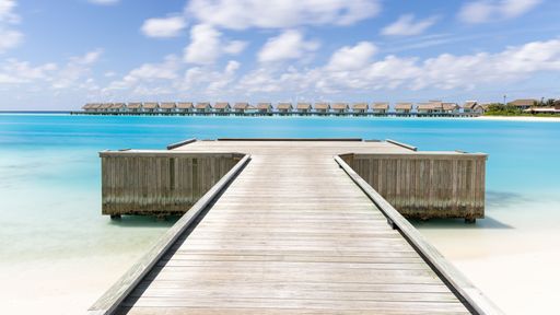 Stunning view of a wooden pier extending into the bright turquoise water of a peaceful ocean in the Maldives