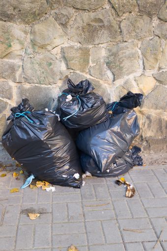 A vertical picture of three black trash bags under the sunlight against a wall