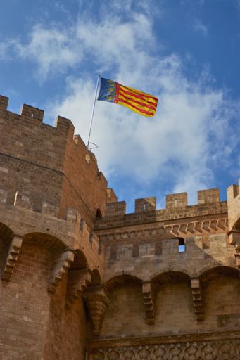 Close up shot of the flag of the Valencian Community and city of Valencia blowing in the wind on top of the amazing Torres de Serranos