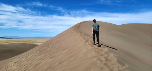 A person stands atop a picturesque sand dune in the beautiful desert landscape of Great Sand Dunes National Park