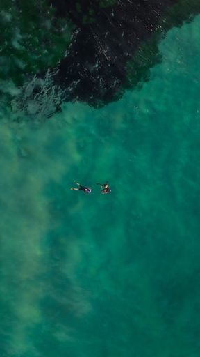 Two people enjoying the sun and waves, standing on their surfboards and paddling in the picturesque blue ocean