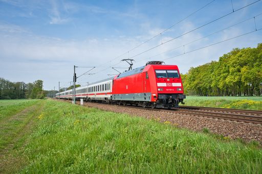 A red, electric train traveling through a scenic rural landscape in Gross Kreutz, Germany
