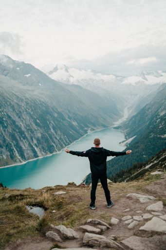 A vintage image of a man atop a majestic peak, admiring a fog-clad mountain range and a serene blue river