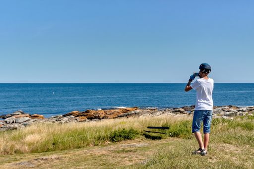 A teenage boy wearing cycling helmet taking photos of a beautiful view of Baltic Sea with his smartphone in Svaneke, Bornholm, Denmark