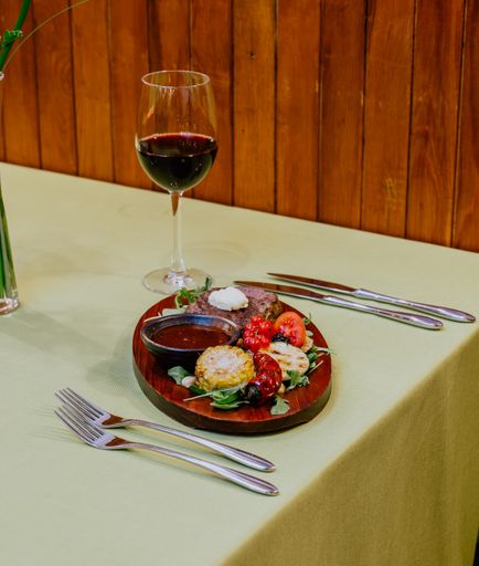 A vertical shot of dinner with cutlet, steak, a sauce, fruits, and vegetables served with wine