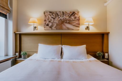 A hotel bedroom with a picture and lamps on the wall, nightstands with plants