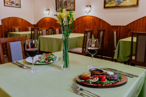 A dining restaurant table with fresh dishes, glasses of red wine for two, and decorative flowers