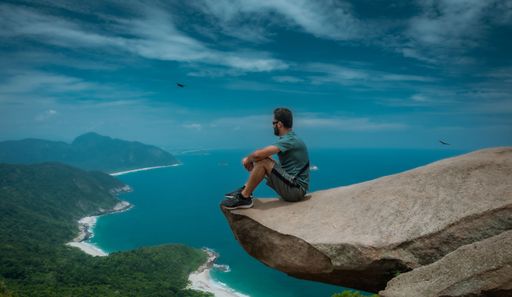 A man sitting on the edge of a cliff admiring the beautiful ocean view, Pedra do Telegrafo, Rio de Janeiro, Brazil