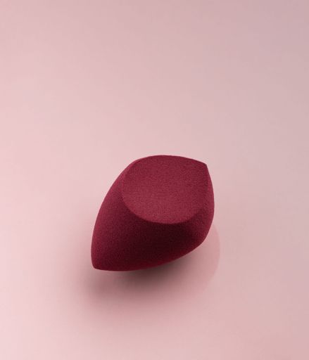 The Red cosmetic sponge in the shape of an egg on a pink background